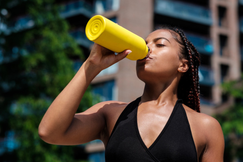 Woman drinking from reusable yellow water bottle