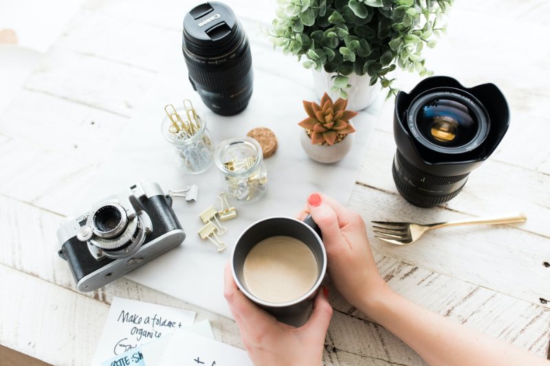 Holding coffee with camera and camera lens besides