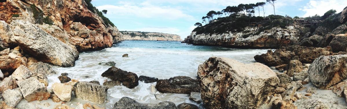 Panoramic view of Calo des Moro beach in Mallorca, Spain, featuring rugged cliffs, turquoise waters, and clear blue sky.