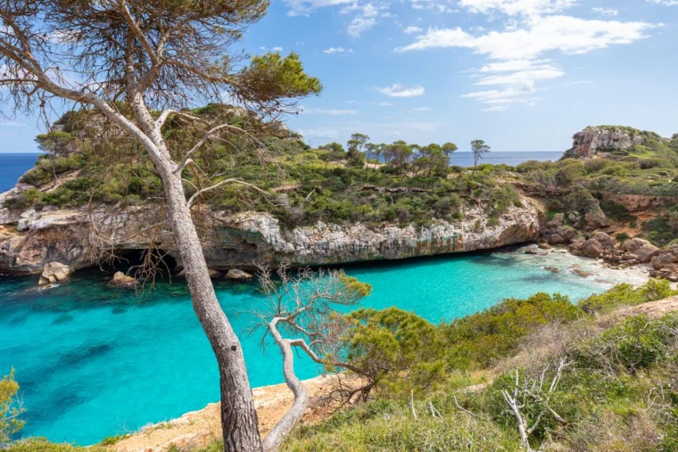 Es Caló des Moro beach in Mallorca's Balearic Islands, Spain—serene cove near Santanyí, featuring turquoise waters, rugged cliffs, lush greenery.