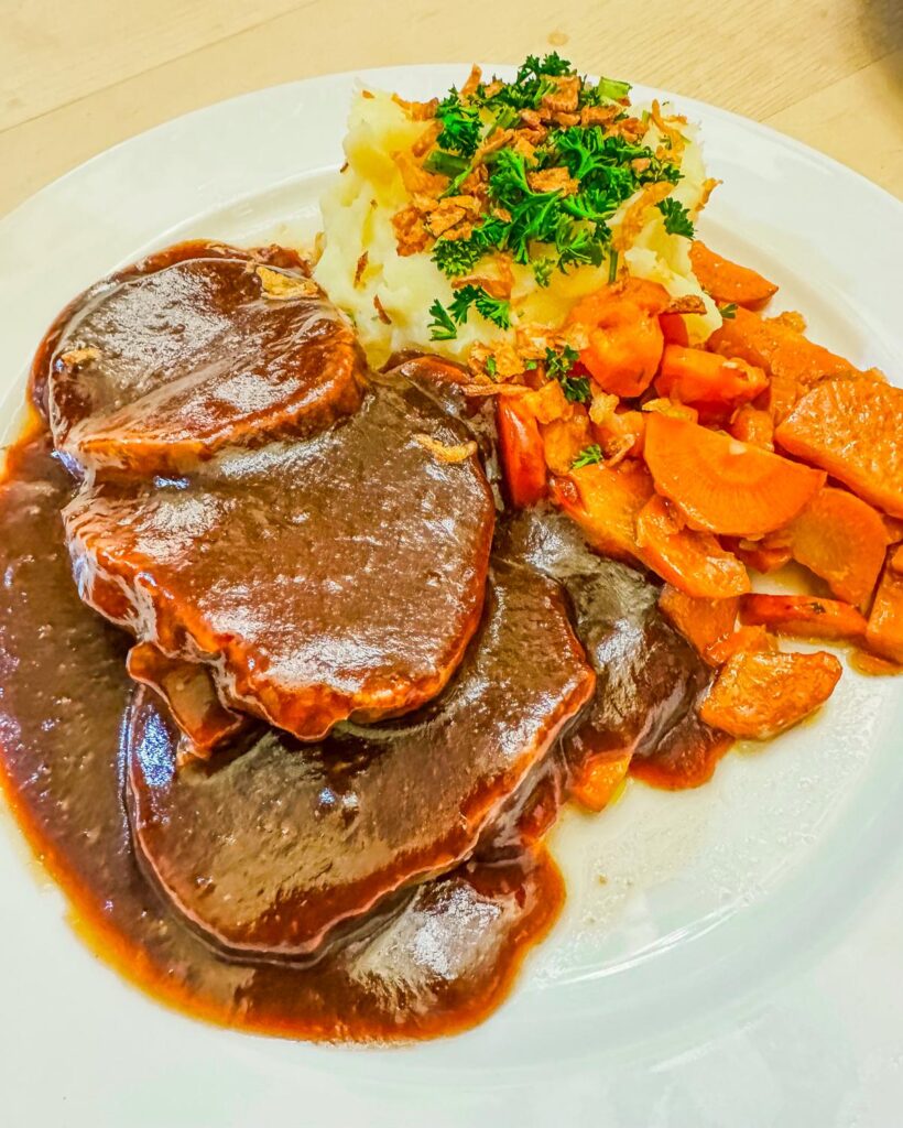 Close-up of traditional German Sauerbraten with mashed potatoes, glazed carrots.