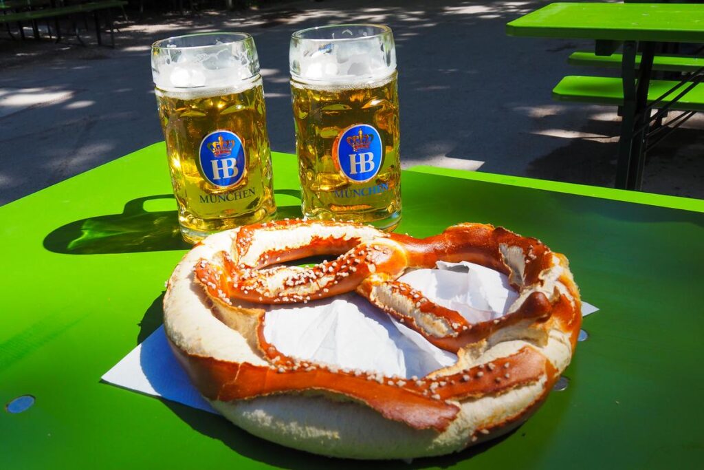 Authentic Bavarian beer garden experience with giant pretzel and beer steins in Munich's Chinesischer Turm.