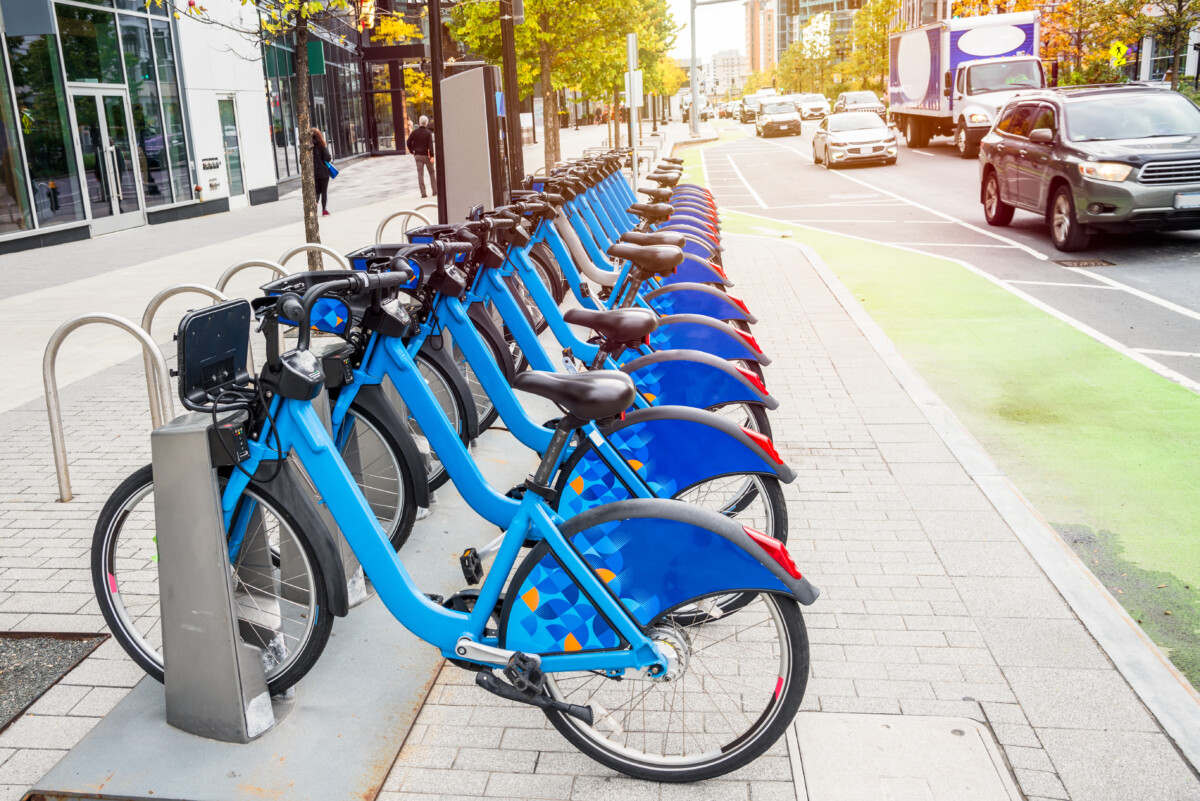 Share-use bicycles in a docking station along busy street with a bike lane in a downtown