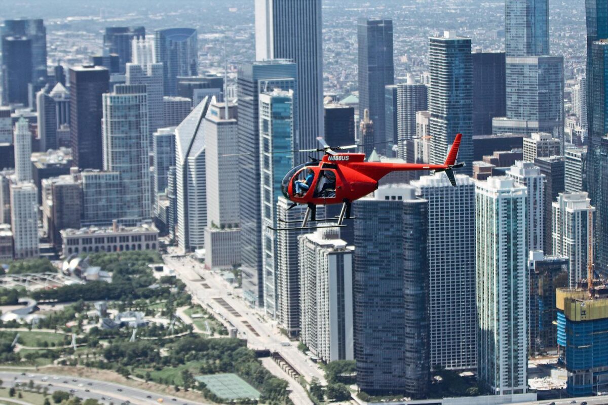 Red Helicopter flying through Chicago, with skyscrapers in the background.