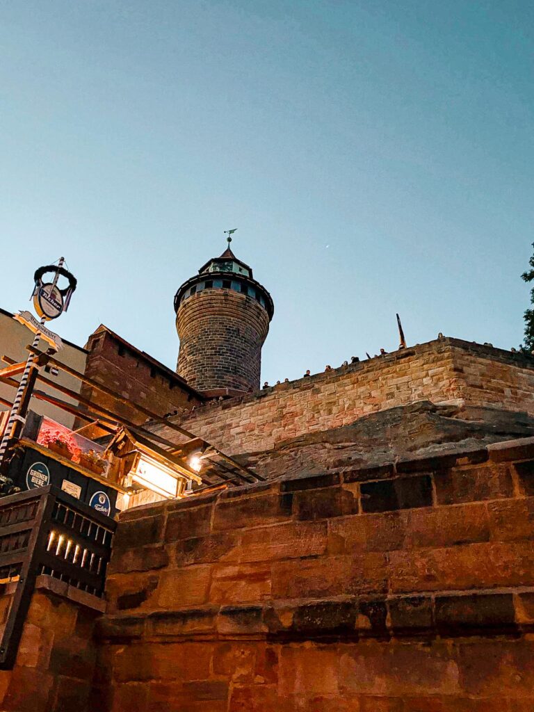 Night-time photo of Imperial Castle of Nuremberg, showcasing sturdy stone architecture and medieval tower against dusky sky.