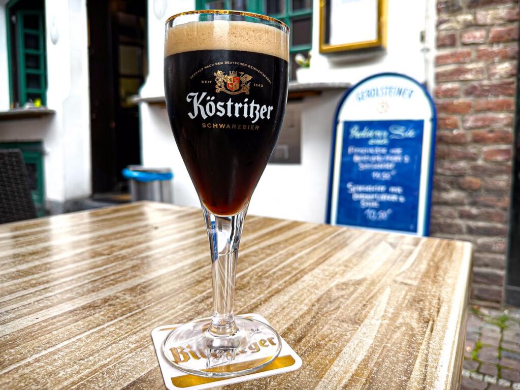 High-res image of impeccably poured Köstritzer Schwarzbier in branded glass at authentic outdoor European bistro