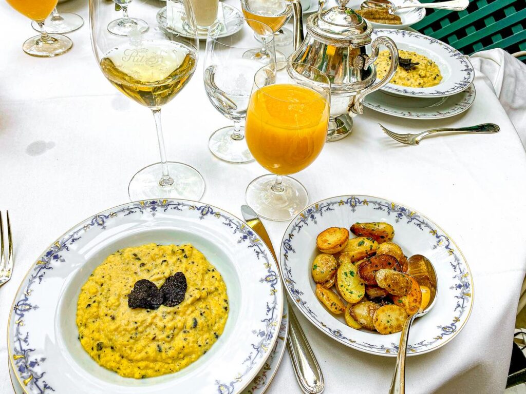 Luxurious brunch spread at Ritz Paris showcasing French cuisine with truffle eggs, roasted herb potatoes, and champagne.