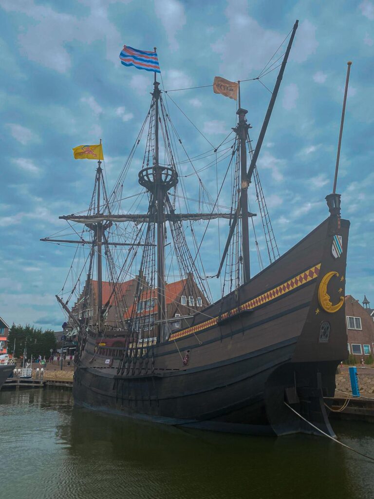 Alt text: Vintage wooden sailing ship in Volendam Harbor with Dutch flag, traditional architecture in background.