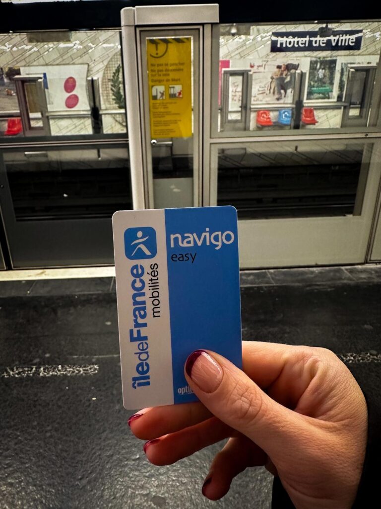 Navigo Easy Metro card being displayed in a commuter's hand at Hôtel de Ville Metro station in Paris.