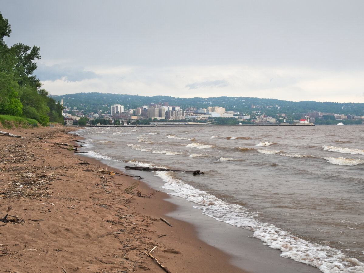 Park Point Beach with driftwood on Lake Superior with Duluth, Minnesota in background under cloudy sky