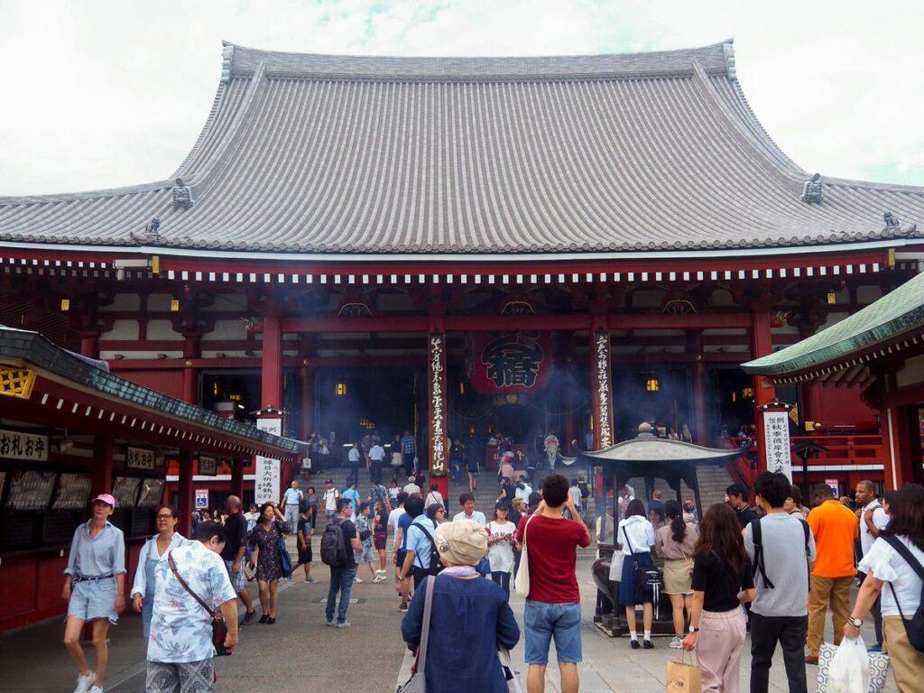 Senso-ji Temple in Asakusa, Tokyo: tourists and locals engage in activities, offering prayers and soaking in history under a clear sky.