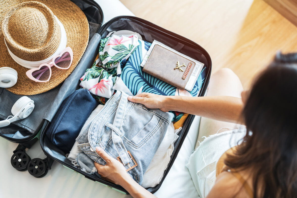 A woman is seated on the bed, organizing her suitcase.